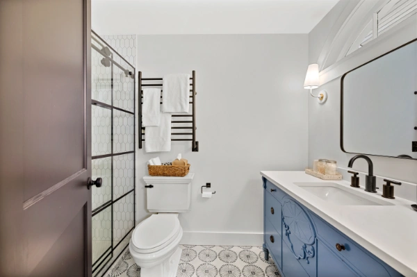 Bathroom interior with patterned tile flooring, glass shower enclosure, blue vanity, black fixtures, and wall-mounted towel rack